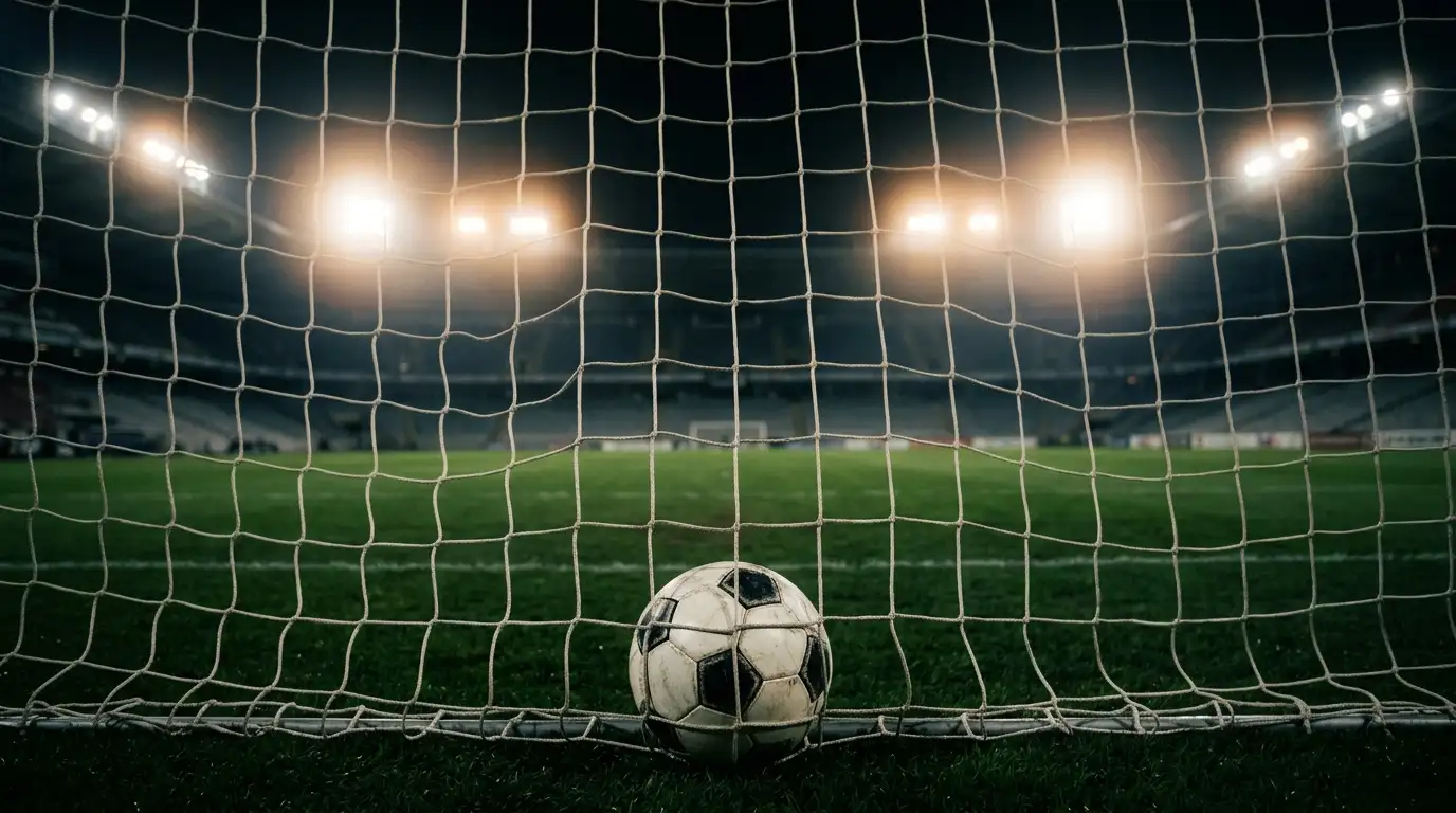 Een voetbal in het net van een leeg doel onder stadionverlichting